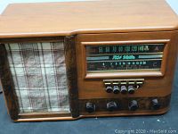 Full view of vintage RCA Victor tube radio showing wooden cabinet, plaid cloth speaker grille, tuning dial, and knobs.