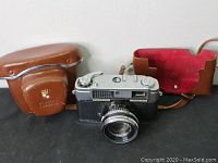 Camera and matching brown leather carrying case with strap, both shown from front angle on black surface.