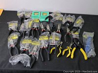 Full view of all hand tools laid on black surface including over 20 pliers and one wrench mostly in packaging.