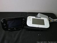 White Wii U console and two Wii U gamepads (black and white) powered on and displayed on TV, connected to Wii U power charger.