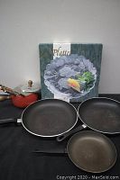 Three frying pans with signs of use laid out on black surface with a serving tray behind.