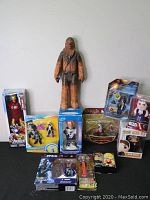 Overview showing a large Chewbacca figure, boxed Iron Man figure, Star Wars item in box, Narnia snow globe, and various other collectibles and figures.