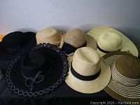 Seven assorted hats laid out on a flat surface showing variety of colors and styles.