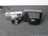 Canon Canonet QL19 camera and carrying case side by side on a black surface