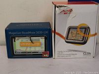 Boxes of Magellan RoadMate 3030-LM and Mio C220s with clear branding and model names.