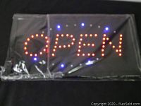 Photo showing LED open sign lit up with red and blue LED lights, wrapped in plastic.