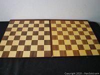 Two foldable wooden chess boards laid open on a black surface, showing the checkerboard patterns of squares.