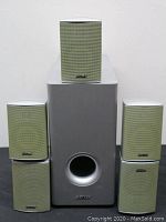 Daytek 5.1 speaker system with one subwoofer and five satellite speakers arranged with the subwoofer in the center and satellites around it.