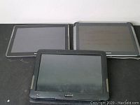 Three Samsung Galaxy Tab 2 tablets, two without cases side by side and one in a black protective textured case in front.
