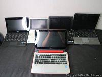 Front view showing five laptops in a row, including ASUS, HP, Samsung, white mini-laptop, and a black laptop.