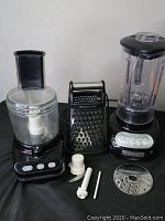 Three KitchenAid kitchen items: black food processor with clear bowl and blade attachment, black blender with clear pitcher, black handheld box cheese grater with storage compartment.