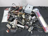 Top-down photo showing a large pile of assorted car audio parts with wiring harnesses, connectors, mounting brackets, and fuse holders.