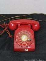 Front view of the red rotary phone showing handset and dial.