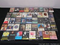 40 audio cassette tapes arranged in rows on a black surface, showing front covers with various album artworks and artist names.