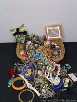 Overview of assorted costume jewelry in a wicker basket and spread out, showing various types such as bracelets and necklaces with diverse colors and materials.