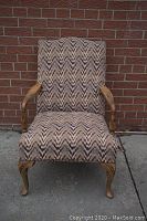 Full view of the antique wooden armchair with patterned zigzag fabric upholstery, showing shape and condition.