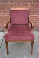 Front view of the antique armchair showing the burgundy cushioned seat and backrest within a wooden frame.