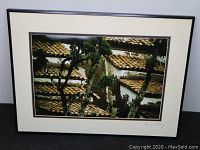 Framed photograph showing tree and tiled roofs with signature of the artist Brian Mantrop in bottom right corner.