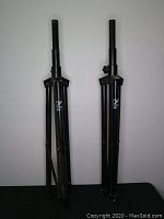 Pair of Yorkville SKS11B black tripod speaker stands folded and standing upright against a white background.
