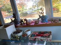 Photo shows assorted garden pots, a duck decoy, glass potpourri bowl, mermaid and schnauzer figurines on a table and window ledge.