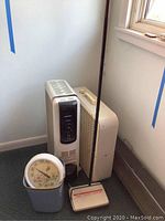 Overview photo showing all items grouped together in corner: heater, fan, carpet sweeper, trash bin, outdoor thermometer