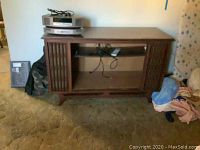 Front view of wooden TV stand with electronic equipment on top and inside shelf visible through glass door. Left side decorative panel visible.