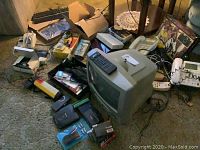 Photo of CRT TV with VHS player, Sony Dream Machine, Nikon camera box, telephones, and other electronics on carpet floor