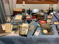 Wide shot of lot items on blue cloth showing jewelry boxes, watches, ties, lighter, multitool and assorted accessories.
