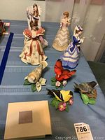 Overall display of Lenox princess figurines, four Lenox bird figures with one chip, and Mikasa picture frame on a blue tablecloth.