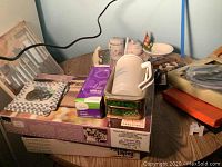 Various items including Apple clock in metal frame, boxed cutlery sets, trivets, and miscellaneous kitchen items on table.