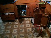 Wood cabinet with doors open displaying pots, pans and other kitchen items inside.