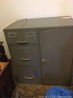 Front view of gray metal file cabinet with three drawers on the left and locking side door on the right.