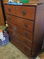 Full front view of the vintage dresser showing its medium brown wood finish, five drawers, and ornate metal drawer pulls