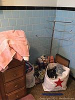Image showing pink towels on a wooden dresser next to a metal towel rack and a bag with multiple boxed household items inside.