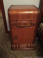 Full front view of the vintage nightstand showing waterfall edges, carved drawer front with geometric and leaf motifs, and decorative knob on cabinet door.
