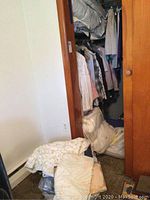 Closet with folded wool blankets, linens stacked on floor and closet top shelf beneath hanging clothes