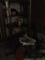 Dark photo showing shelving with assorted items, tools, and containers including what appears to be the leaf blower and other equipment.