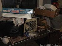 Magic Show box on top of a white tray, surrounded by fabric textiles, storage crates, and boxes.