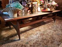 Full side view showing mid century style wooden coffee table with angled legs and lower stretcher, multiple decorative items on top (not included)