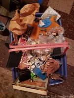 A bin filled with assorted costume jewelry items including necklaces, bracelets, and smaller boxed pieces in plastic and paper wrapping.