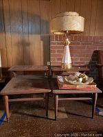 Three brown walnut-finish end tables arranged with a painted table lamp and box of parts