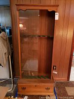 Full front view of the wooden gun cabinet showing the glass sliding door and bottom drawer.