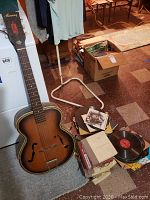 Full view of guitar standing next to box of records