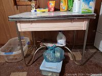 Vintage metal framed table with pull-out leaf, showing rust and soiling, items on and under table excluded from lot