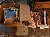 Box containing multiple Playboy magazines, some with blue denim shorts cover and others with photographic covers.