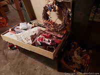Grapevine wreath on top of a box containing various Christmas decorations including candy cane shaped ornaments and fabric figures.
