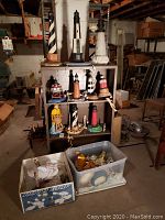 Full view of all lighthouse lamps arranged on shelves and in boxes nearby in basement setting.