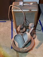 Photo shows portable electric heater with two vintage oil lanterns in front, along with two metal scoops placed inside a metal bowl.