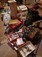 Wide view of assorted Christmas decorations scattered on concrete floor including boxes of candle holders, garlands, string lights, and various boxed and loose Christmas balls.