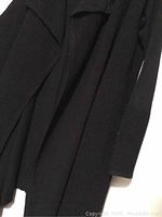 Close-up of black ribbed knit texture sweater sleeve and front edge, showing fabric and design